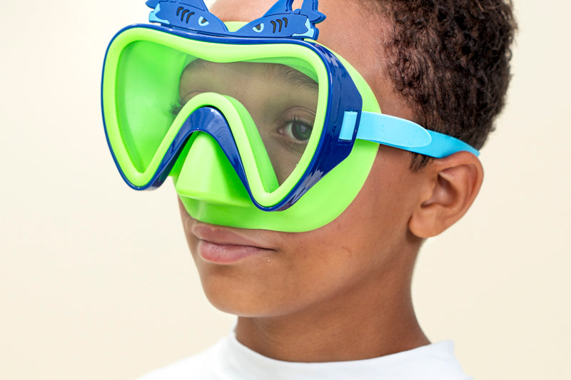 boy smiling wearing blue fish kids' swim mask showing green nose piece and blue frame with two silicone blue fishes above the frame