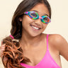 girl smiling wearing rainbow rhinestone kids swim goggles featuring a rainbow colorway with a blue glittering frame, pink nose piece and pink rhinestones