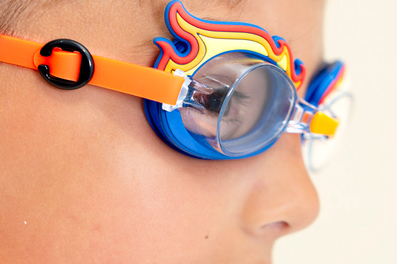 close up image of boy wearing mini flame kids swim goggles showing silicone flame detail on a blue swim goggles with an orange strap and nose piece