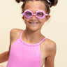 girl smiling wearing mini pink petals kids swim goggles featuring a pink swim goggle with pink petals wrapped around the lenses with a pink strap and nose piece