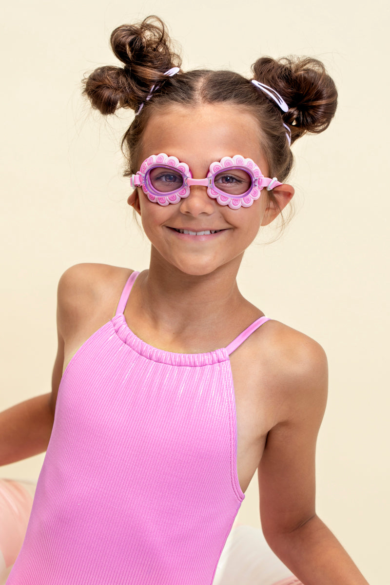 girl smiling wearing mini pink petals kids swim goggles featuring a pink swim goggle with pink petals wrapped around the lenses with a pink strap and nose piece