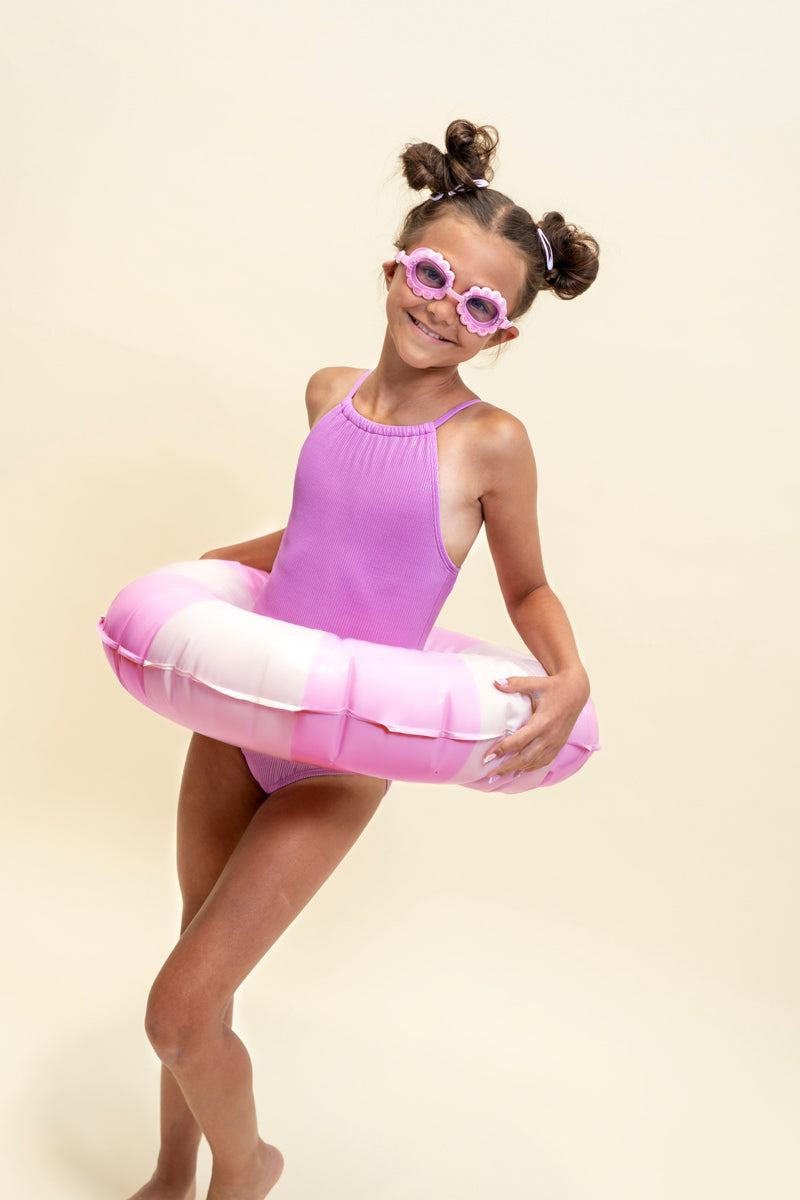 girl smiling and posing with inner tube wearing mini pink petals kids swim goggles featuring a pink swim goggle with pink petals wrapped around the lenses with a pink strap and nose piece