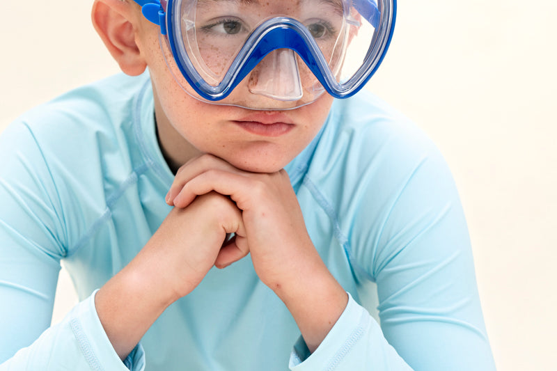 boy posing and wearing splash in color blue kids swim mask featuring a clear gasket and nose covering with a bright blue frame and strap