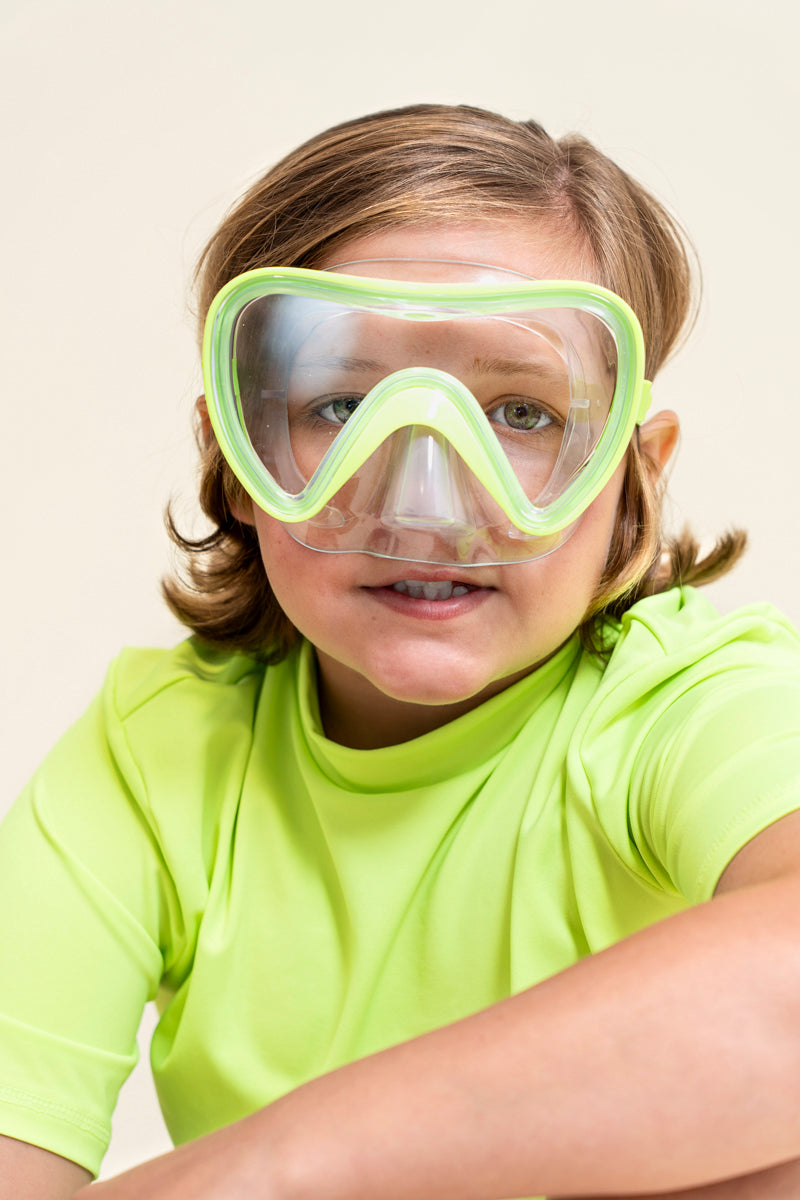 boy sitting smiling wearing splash in color green kids' swim mask showing a clear gasket and nose covering featuring a lime green frame and strap