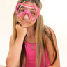 girl sitting and smiling wearing pink splash kids' swim mask featuring a clear gasket and nose covering and bright pink frame and strap