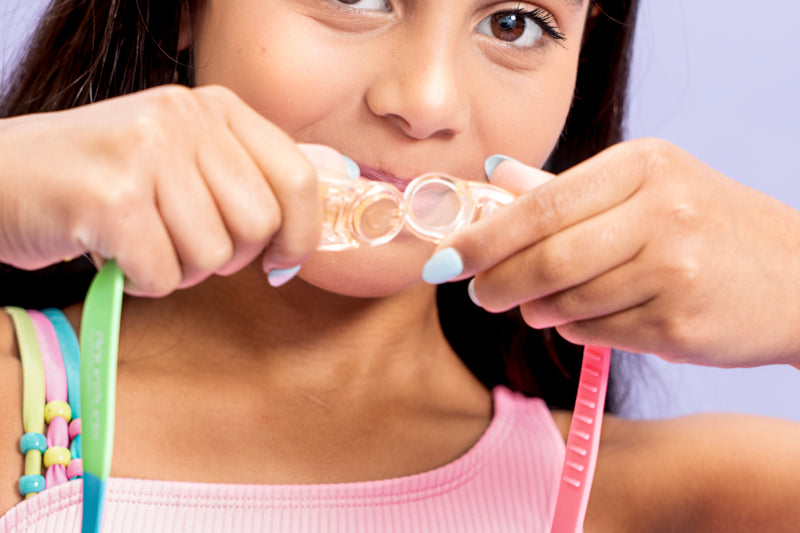 girl showing that the panoramic rainbow kids swim goggles feature a clip in the back that makes it easy to apply minimizing tugging of hair