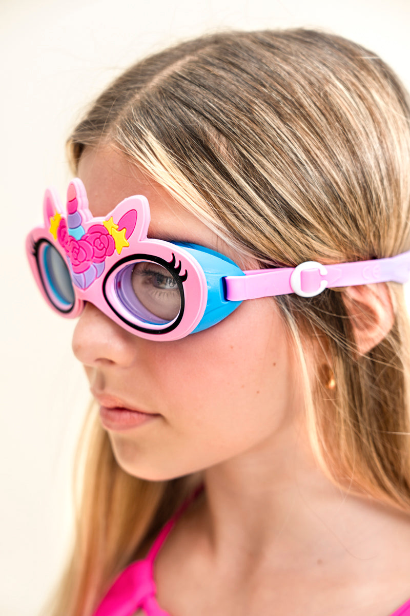 angled photo of girl wearing flex pink unicorn kids swim goggles featuring an all silicone flexible pink frame with a unicorn horn and ears with a flower crown on the silicone. Also featuring a blue gasket and pink strap