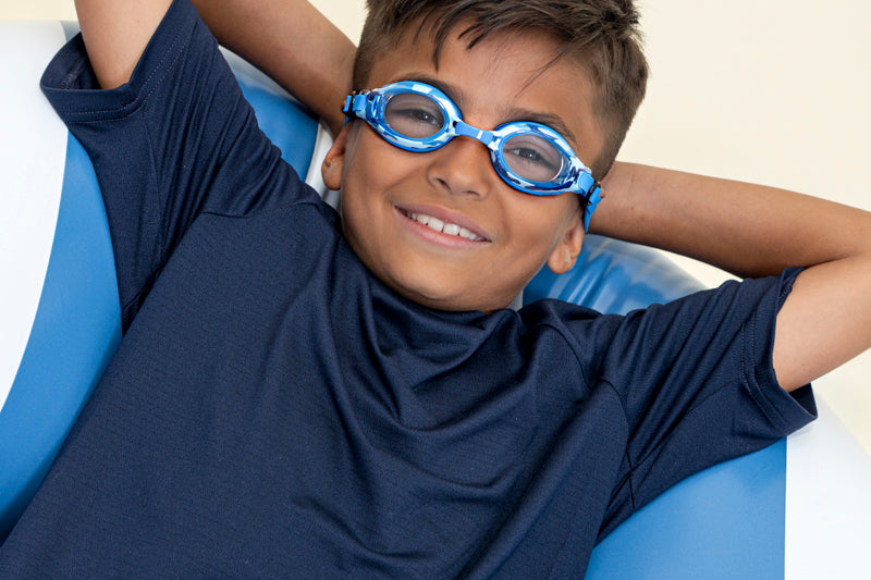 boy laying in inner tube posing wearing blue camo kids' swim goggles which feature a blue camo print on the frame