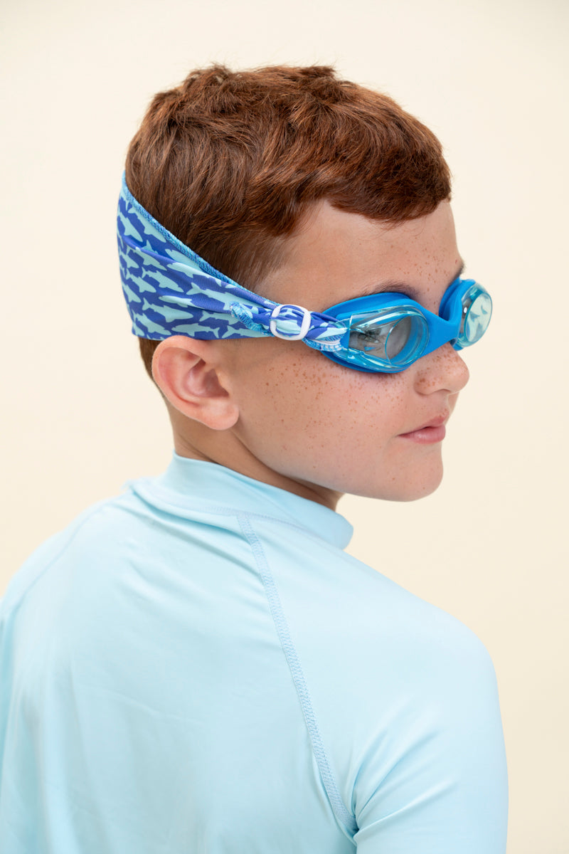 boy wearing soft strap shark blue kids swim goggles which feature a soft strap fanned out across the back of his head. the swim goggles feature a blue swim goggle and royal blue soft strap with light blue shark silhouettes  