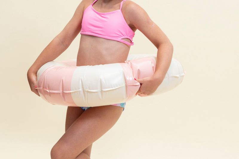 girl posing in an inner tube, smiling wearing mini unicorn kids swim goggles which feature  a silicone unicorn decoration wrapping around the top of the frame on a purple gasket and blue and pink strap with a pink nose piece