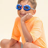 boy sitting and smiling wearing mini race car kids swim goggles which feature a blue swim goggle with silicone race car decorations across the top of both lens with a grey strap and red nose piece